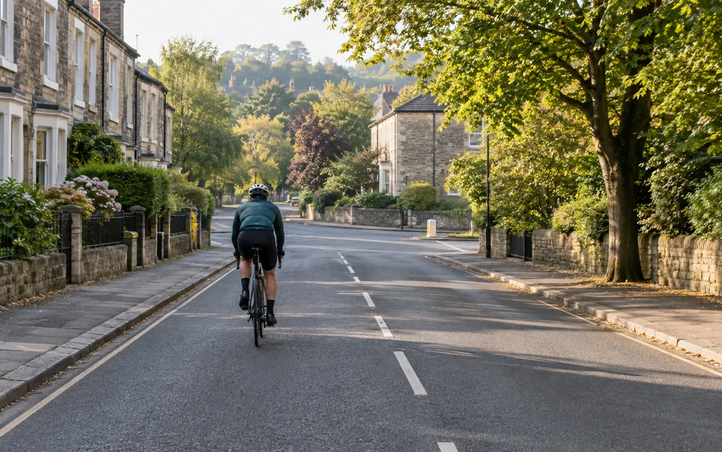 A cyclist seen from behind riding confidently in the centre of a quiet lane on a tree-lined British town street